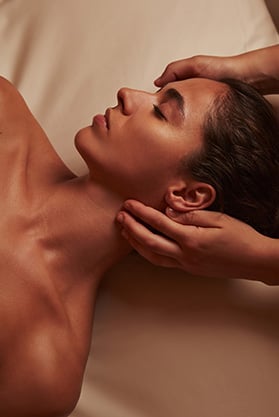 A woman with a relaxed expression getting a facial massage.