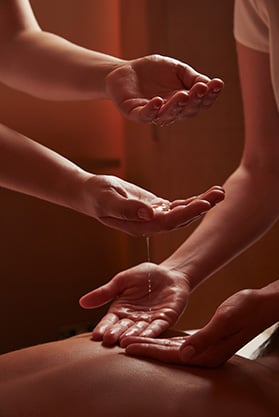 Four outstretched hands with oil dripping down onto a person's back for the four hands synchronised ceremony massage