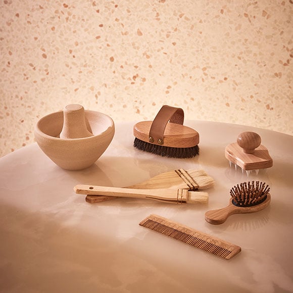 An arrangement of natural wooden spa tools on a polished white onyx surface, including brushes, a wooden comb, and a massage tool. The minimalistic setting creates a soothing atmosphere, enhancing the serene experience of a luxury treatment