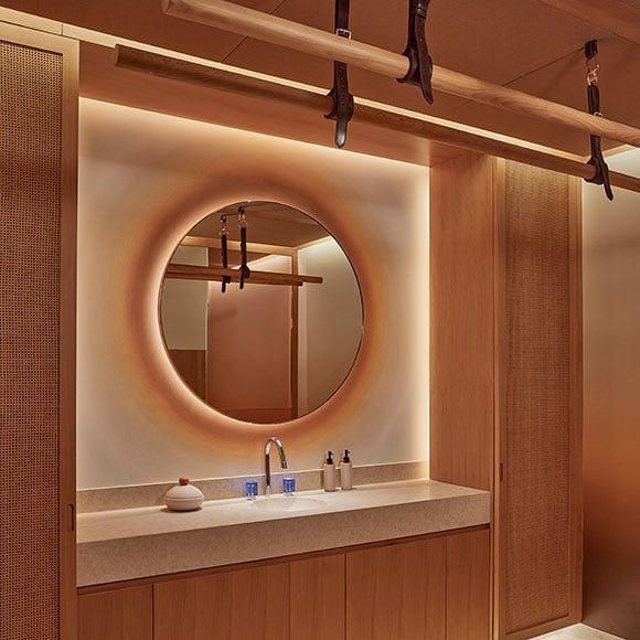 Glowing spa treatment room. A mirror is hung on the back wall facing a massage bed. The room features wooden wall panelling and a marble sink